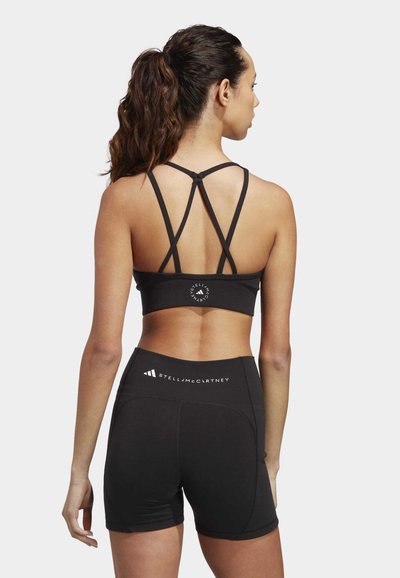 Black sports bra with crisscross straps and logo detail, paired with high-waisted black shorts featuring branding on the waistband.