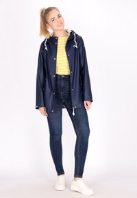 Jūras spēku ūdensizturīga lietus jaka ar kapuci, sudraba spiedpogām, pelēku oderi, apvienota ar dzeltenu svītrainu krekli un ziliem šauriem džinsiem.