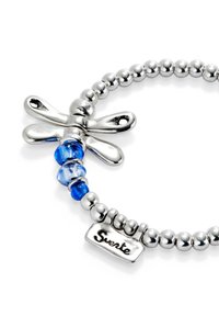 Bracelet en perles d'argent avec un charme libellule, des perles en verre bleu et une étiquette en métal gravée "Suerte". Textures mates et brillantes.