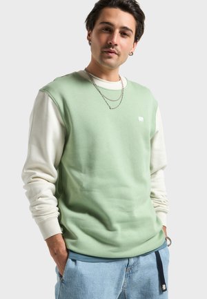 Sweat-shirt vert à col rond avec manches longues blanches, arborant un petit logo blanc. Tissu doux, coupe décontractée, poignets côtelés et forme classique.
