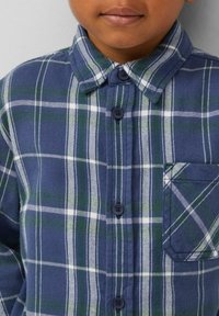 Blauwe en groene geruite flanellen shirt met een knoop-sluiting, kraag en borstzak. Heeft donkere knopen en een zachte textuur.