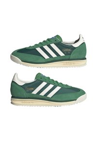 Zapatillas de ante verde y nylon con rayas blancas, que presentan un diseño retro y una marca dorada en el costado. Suela de goma con tracción texturizada.