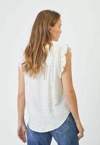 Camicia bianca con maniche a volant e dettagli in pizzo. Tessuto morbido e testurizzato, vestibilità rilassata, orlo curvo e design posteriore sobrio.