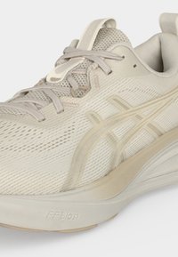 Chaussure de course beige clair avec tige en mesh, fermeture à lacets, semelle rembourrée et design texturé, avec marquage « FF Blast » sur la semelle.