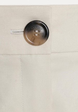 Nasture rotund de culoare maro închis cu patru găuri prins pe o țesătură bej, în apropiere fiind cusută o găură pentru nasture.