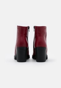Rote Leder-Ankle-Boots mit einer glatten Oberfläche, ausgestattet mit seitlichen Reißverschlüssen und gerippten schwarzen Absätzen für zusätzlichen Halt und Unterstützung.
