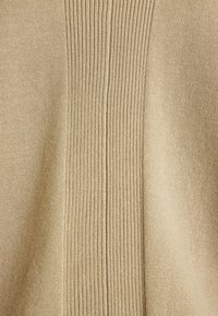 Beige stickad tröja med ribbad текстur och en mittsöm. Slät tyg på vardera sidan skapar en subtil kontrast i mönstret.