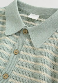 Svetlo modra pletena polo majica s teksturirano tkanino, s horizontalnimi kremnimi črtami, ovratnikom in rjavimi gumbi.