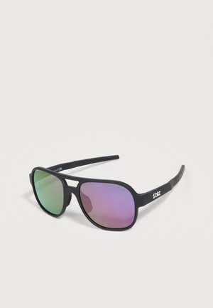 Gafas de sol con montura negra, lentes verdes y moradas espejadas y el logo "bliz" en la patilla, colocadas sobre una superficie gris clara.