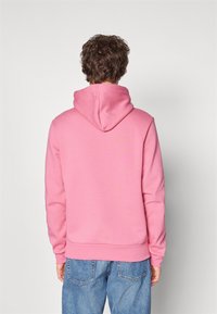 Felpa in cotone rosa con cappuccio regolabile, polsini e orlo a coste, abbinata a jeans azzurri chiari. La vista posteriore mette in evidenza un design semplice.
