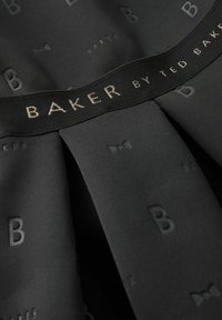 Czarna sukienka z tkaniny z delikatnym wzorem liter i kokard, z czarnym pasem oznaczonym napisem "BAKER BY TED BAKER" w metalicznym wykończeniu.