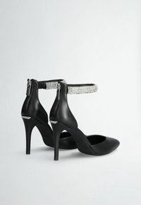 Scarpe nere con tacco alto, punta affusolata, realizzate in pelle liscia, con un cinturino alla caviglia decorato da cristalli e chiusura con zip.