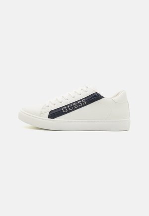 Sneaker bianche con finitura in pelle liscia, dotate di una striscia blu navy e branding "GUESS". Punta rotonda, suola piatta e design con lacci.
