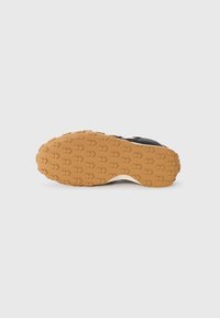 Black sports shoe with a textured brown rubber sole featuring arrow-shaped patterns for traction and stability.