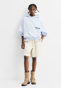 Felpa oversize azzurra con stampa "LOS ANGELES", pantaloni corti beige con vita a righe, e stivali alla caviglia taupe con dettagli a cinturino.