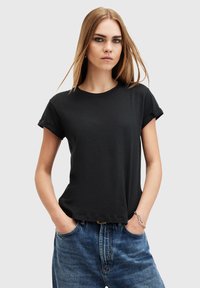 Černé bavlněné tričko s krátkými ohrnutými rukávy, kulatým výstřihem a volným střihem, nošené s modrými džíny s vysokým pasem.