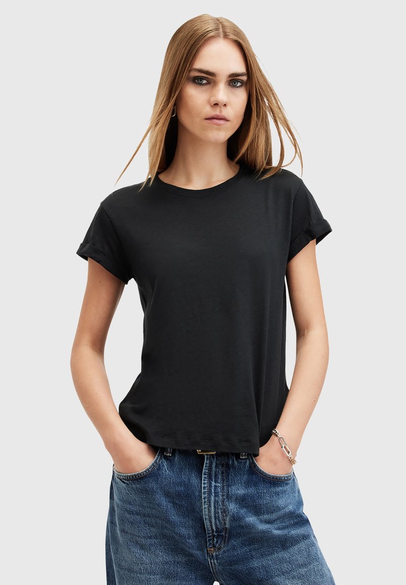 Černé bavlněné tričko s krátkými ohrnutými rukávy, kulatým výstřihem a volným střihem, nošené s modrými džíny s vysokým pasem.