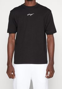T-shirt nera a maniche corte con scollo rotondo, con logo testuale "Hugo" bianco sul petto. Realizzata in morbido cotone.