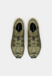 Αθλητικά παπούτσια ελιάς με καουτσούκ σόλα, υφή στην επιφάνεια και ενσωματωμένο σύστημα κορδονιών. Εντυπωσιακά σχέδια στα πλάγια.