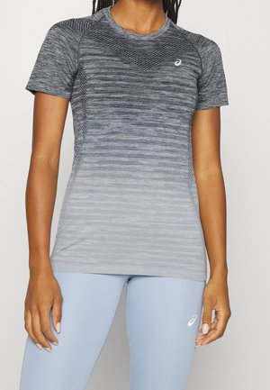Vrouw draagt een nauwsluitend, kort mouw grijs sporttopje met verloopmotieven en lichtblauwe leggings met een klein wit logo.
