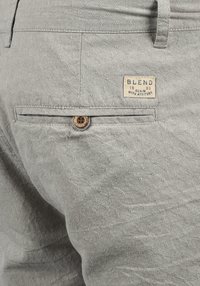 Tissu texturé gris clair avec un motif de diamant subtil. Comprend une poche arrière avec un bouton en bois et une étiquette indiquant "BLEND".