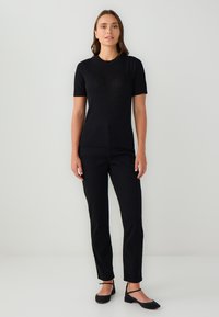 Top nero a maniche corte in design aderente, abbinato a pantaloni neri slim-fit e scarpe basse. Texture liscia con una leggera lucentezza.