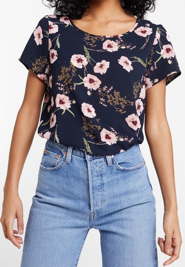 Femme portant un chemisier bleu marine à manches courtes avec un imprimé floral rose rentré dans un jean taille haute bleu clair.