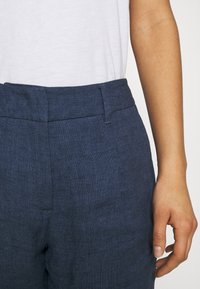 Pantalon en lin bleu marine avec une taille ajustée, présentant un design épuré et une texture subtile. La ceinture a une finition propre et lisse.