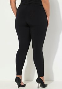 Leggings neri realizzati in tessuto elastico con una superficie liscia, dotati di una vita alta e di una vestibilità aderente, abbinati a tacchi alti neri.