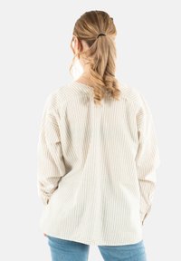 Beige, gestreiftes Langarmhemd mit entspannter Passform, breitem Ausschnitt und leicht gerafften Ärmeln. Kombiniert mit hellblauen Jeans.