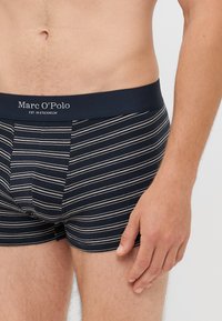 Boksarice z mornarskimi črtami iz bombaža. Opremljene z temnim pasom, na katerem je v beli barvi napis "Marc O'Polo". Mehka tekstura, prilegajoč dizajn.
