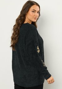 Czarny, puszysty sweter o luźnym kroju, zdobiony złotym haftem w kwiaty na rękawach. Długie rękawy, miękka tekstura i okrągły dekolt.
