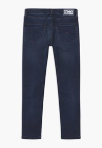 Ciemnoniebieskie dżinsy o slim fit, z tylnymi kieszeniami, widoczną metką w pasie oraz subtelnymi detalami w przeszyciach.