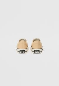 Bež platnene tenisice s niskim dizajnom, crnim detaljima na potplatu i brendingom "CONVERSE ALL-STAR" na peti.