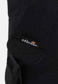 Sangle de sac à dos en tissu noir avec un logo brodé et des accents rouge et jaune. Comprend une boucle en plastique pour l'ajustement.