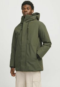 Chaqueta verde con capucha, con cremallera frontal, cordones ajustables y dos bolsillos laterales. Hecha de un tejido suave y resistente al agua.