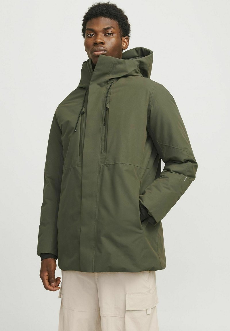 Chaqueta verde con capucha, con cremallera frontal, cordones ajustables y dos bolsillos laterales. Hecha de un tejido suave y resistente al agua.