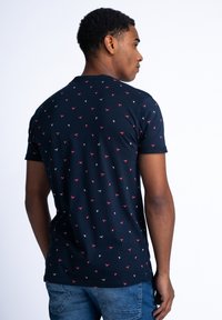 Tmavě modré tričko s krátkým rukávem vyrobené z bavlny, s rozptýleným geometrickým vzorem v červené a bílé barvě, s kulatým výstřihem a volným střihem.