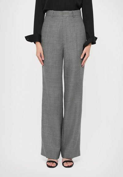Donna che indossa pantaloni grigi a vita alta e gamba larga abbinati a una blusa nera a maniche lunghe e sandali neri open-toe.