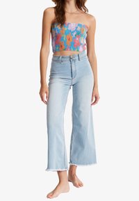 Top corto de tubo colorido con patrón floral combinado con unos jeans de pierna ancha de lavado claro de cintura alta, con detalles de dobladillo sin terminar.