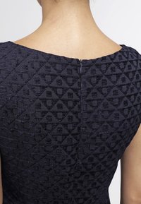 Granatowa sukienka z tkaniny o fakturze w romby, zaokrąglonym dekoltem i zamek z tyłu.