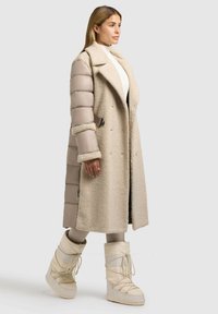 Gara bēša mēteli ar pūkainu ārējo audumu un gludām oderētām piedurknēm, ar izgrieztu apkakli, dubultā pogojuma dizainu un sānu kabatām.