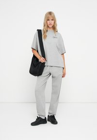 Camiseta gris de gran tamaño con mangas cortas y logo, combinada con joggers grises y zapatillas negras. Mochila negra con correa ajustable.