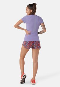 Lila, figursydd kortärmad topp med en strukturadaptering. Matchad med färgglada, blommönstrade shorts. Röda sportskor med svart sula.