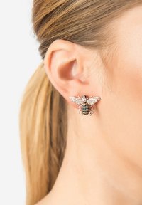 Orecchino a forma di ape in oro rosa con pietre trasparenti e nere, caratterizzato da ali dettagliate e un corpo testurizzato, indossato all'orecchio di un modello.
