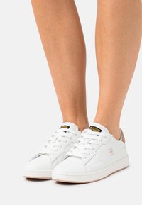 Witte leren sneakers met een gestructureerd oppervlak, platte veters en een tankleurige hakaccent. Voorzien van een zwart en geel logo op de tong.