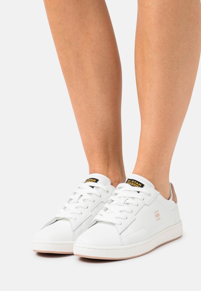 Witte leren sneakers met een gestructureerd oppervlak, platte veters en een tankleurige hakaccent. Voorzien van een zwart en geel logo op de tong.