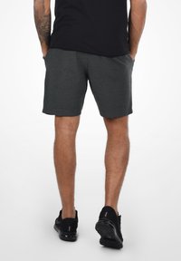 Dark gray athletic shorts with a smooth texture, elastic waistband, side pockets, and a straight cut, paired with black athletic shoes.