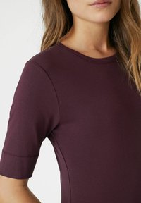Burgundy lyhythihainen paita pehmeästä kankaasta, jossa on pyöreä pääntie. Ominaisuuksiin kuuluu istuva siluetti ja saumatonta olkapäätyötä.