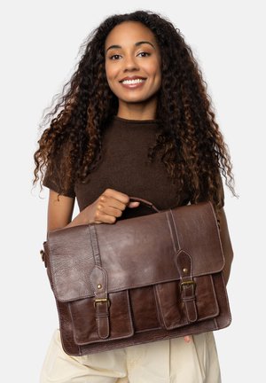 Brown leather messenger bag with a flap, two front pockets, brass hardware, and stitching details. Smooth texture, rectangular shape.